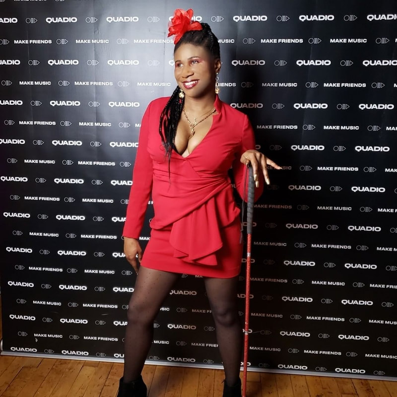 Lachi with cornrows, red dress, red flower and red glamcane cane at red carpet step and repeat , black blind disability female edm singer, actress